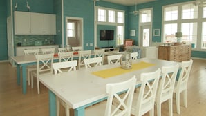 A spacious kitchen with white cabinets and a teal backsplash, large windows, and a ceiling fan.