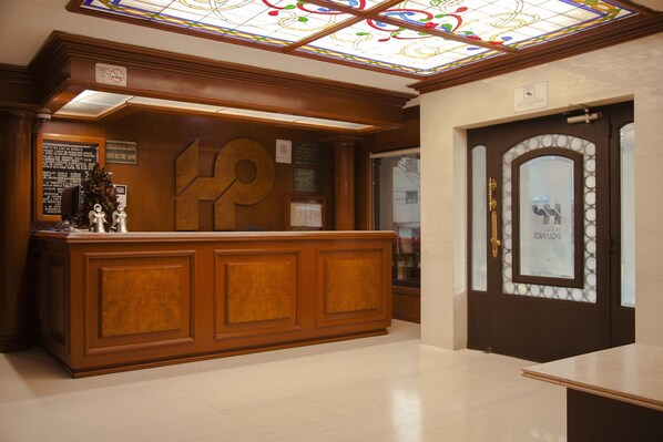Un mostrador de recepción con detalles de madera, un techo de vitrales y una puerta con panel de vidrio esmerilado.