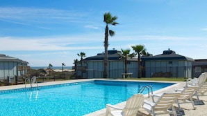Une piscine entourée de chaises longues, de palmiers et de bâtiments en arrière-plan.