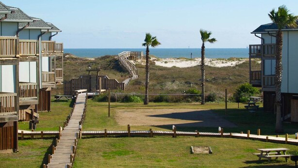 Une propriété située en bord de mer, dotée de terrasses en bois, d’une plage de sable et offrant une vue dégagée sur l’océan.