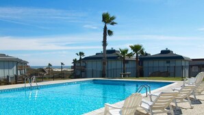 A swimming pool with lounge chairs, palm trees, and buildings in the background. - Turtle Bay 104BH (Port Aransas)