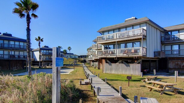 A wooden boardwalk leading to a beachfront property with multiple balconies and picnic tables. - Turtle Bay 104BH (Port Aransas)