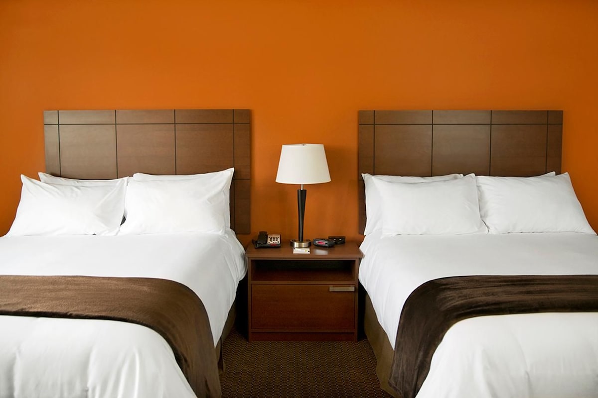A hotel room with two beds, a nightstand with a lamp, and a small table.