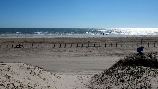 A beach with a sandy shore, a clear blue sky, and a few people walking. - Turtle s Pace SIV5 (Port Aransas)