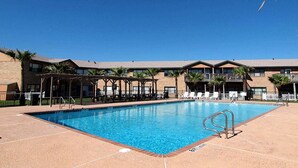 A swimming pool with a clear blue sky, surrounded by a building with multiple balconies and palm trees. - Turtle s Pace SIV5 (Port Aransas)