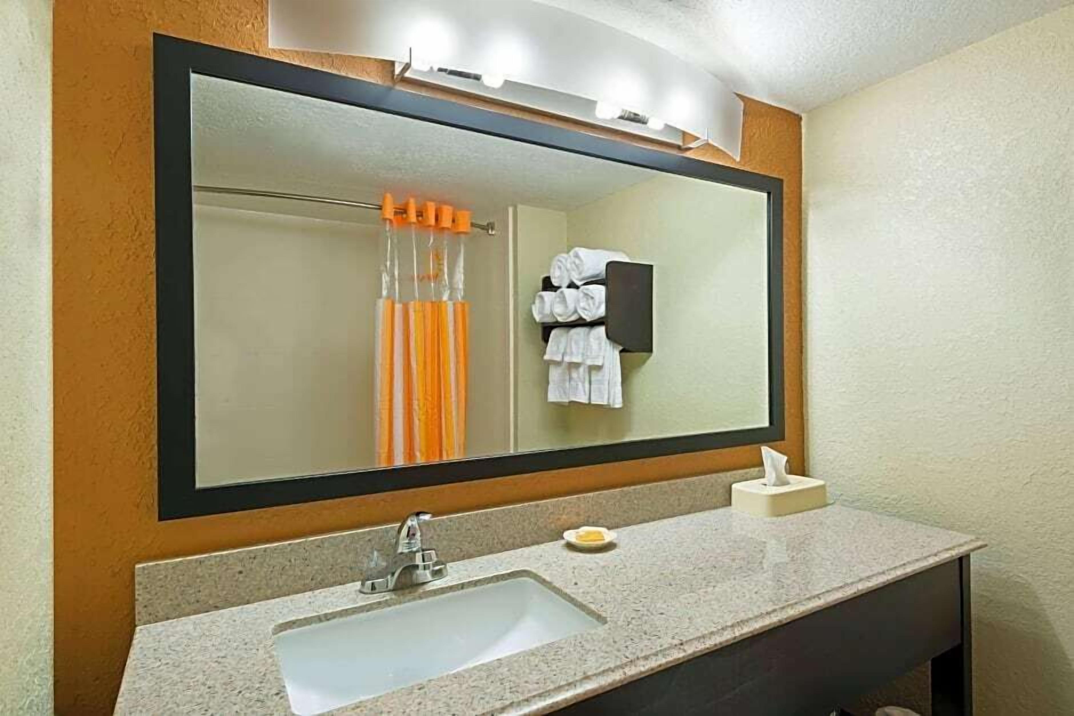 Baño con un espejo grande, un lavamanos y un perchero para toallas.