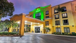 A hotel with a green sign, a covered entrance, and palm trees in the foreground.