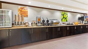 A self-service breakfast station with waffle makers, a coffee machine, and various food containers.