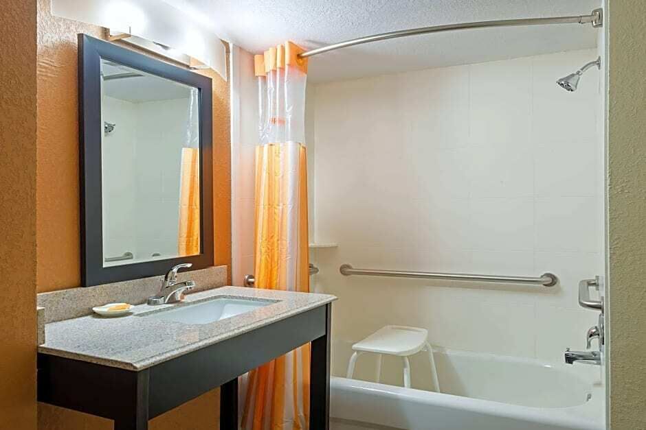 A bathroom with a sink, mirror, shower, and a white stool.