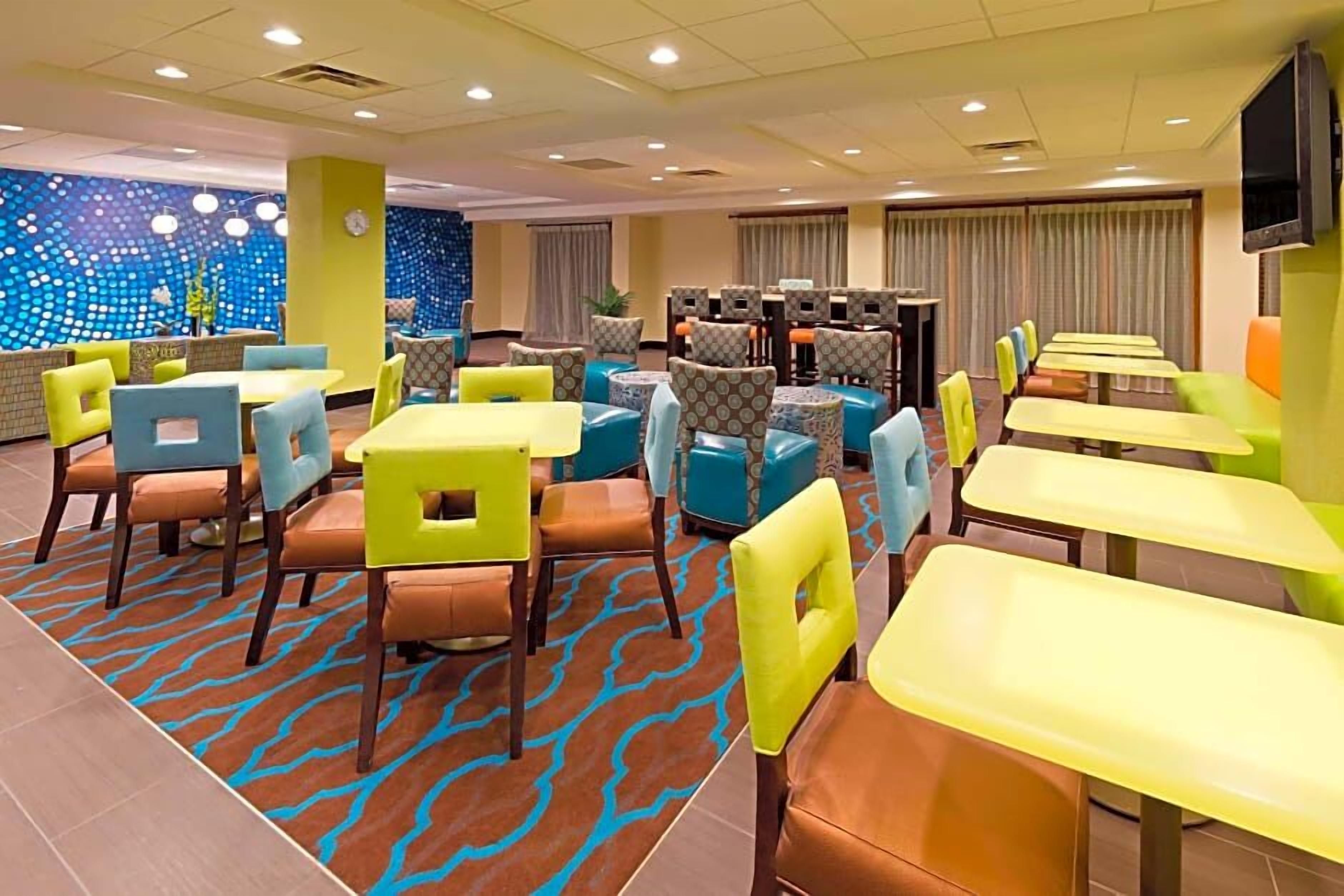 A hotel lobby with multiple seating areas, including tables and chairs, and a patterned carpet.