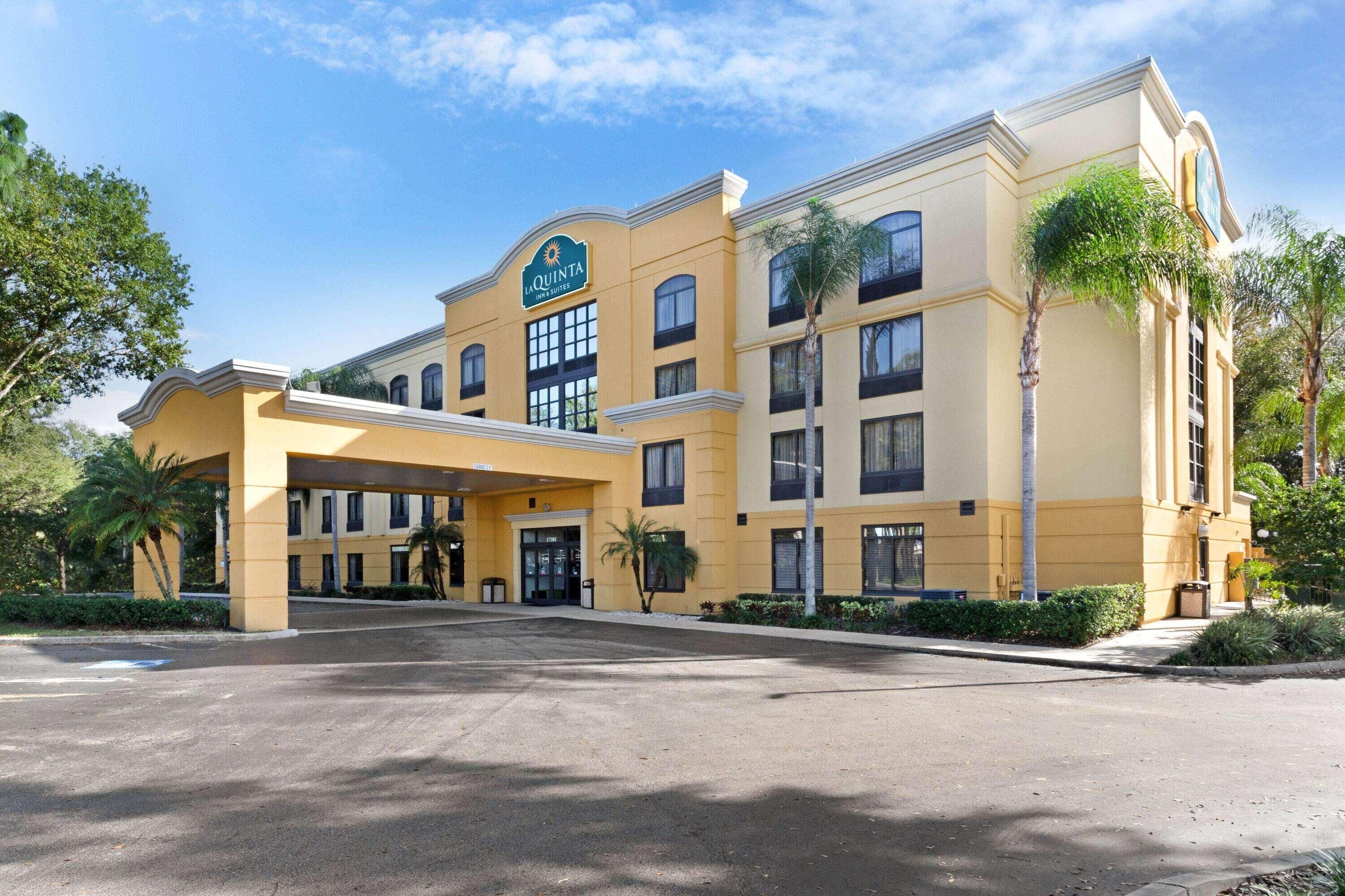 A hotel with a yellow facade, a covered entrance, and palm trees.
