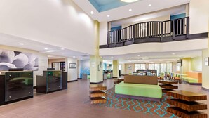 A spacious lobby with a central seating area, a staircase leading to an upper level, and a reception desk.