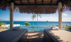 An infinity pool with a view of the ocean, two lounge chairs, and a thatched roof structure. - Raiwasa Grand Villa (Taveuni Island East)