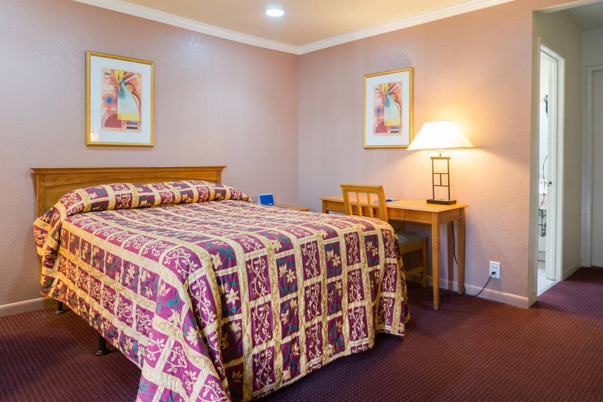A bedroom with a large bed, a desk, and two framed pictures on the walls.