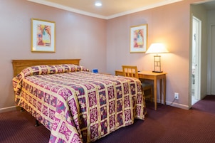A bedroom with a large bed, a desk, and two framed pictures on the walls.