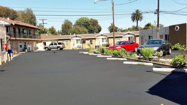 Une vue de rue avec une rangée de bâtiments d’un motel, chacun portant un numéro, un VUS garé et une voiture rouge.