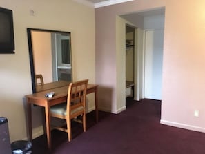A room with a wooden dining table and chairs, a mirror on the wall, and a closet with hanging clothes. - Mission Motel Lynwood (Lynwood)