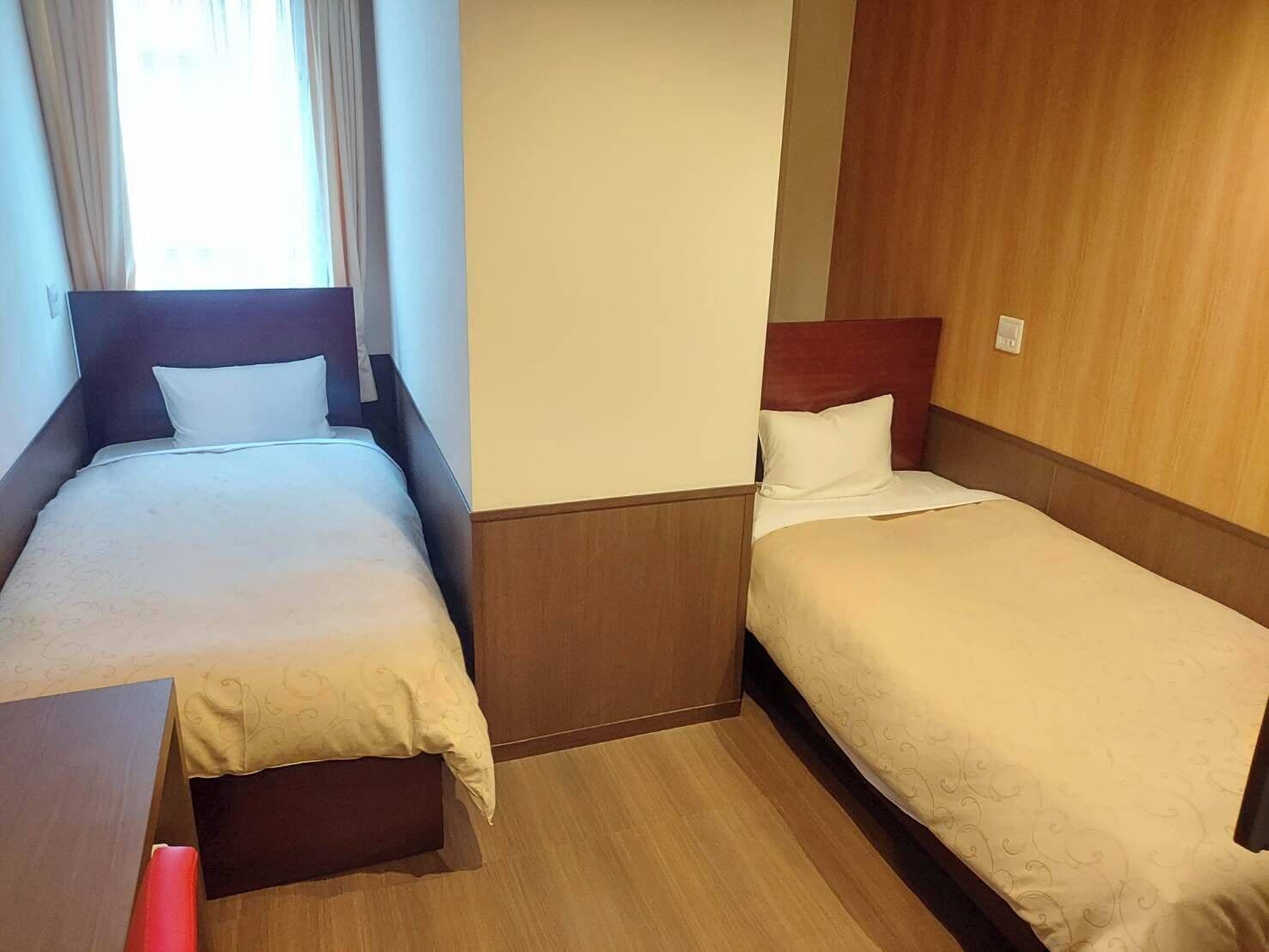 A hotel room with two single beds, wooden headboards, and a wooden floor.
