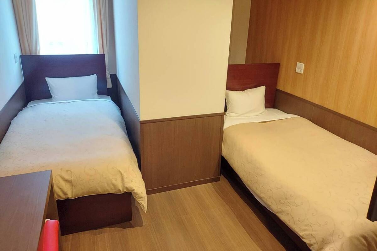 Una habitación de hotel con dos camas individuales, cabeceros de madera y suelo de madera.