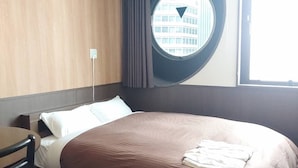 Habitación de hotel con una cama grande, un ventanal redondo con vistas a edificios, un escritorio y una silla.