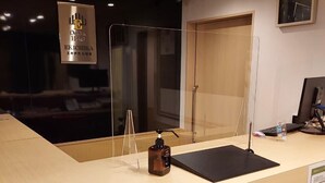 Una recepción de hotel con un reloj digital, un letrero que dice Osaka Hotel y un dispensador de gel antibacterial.