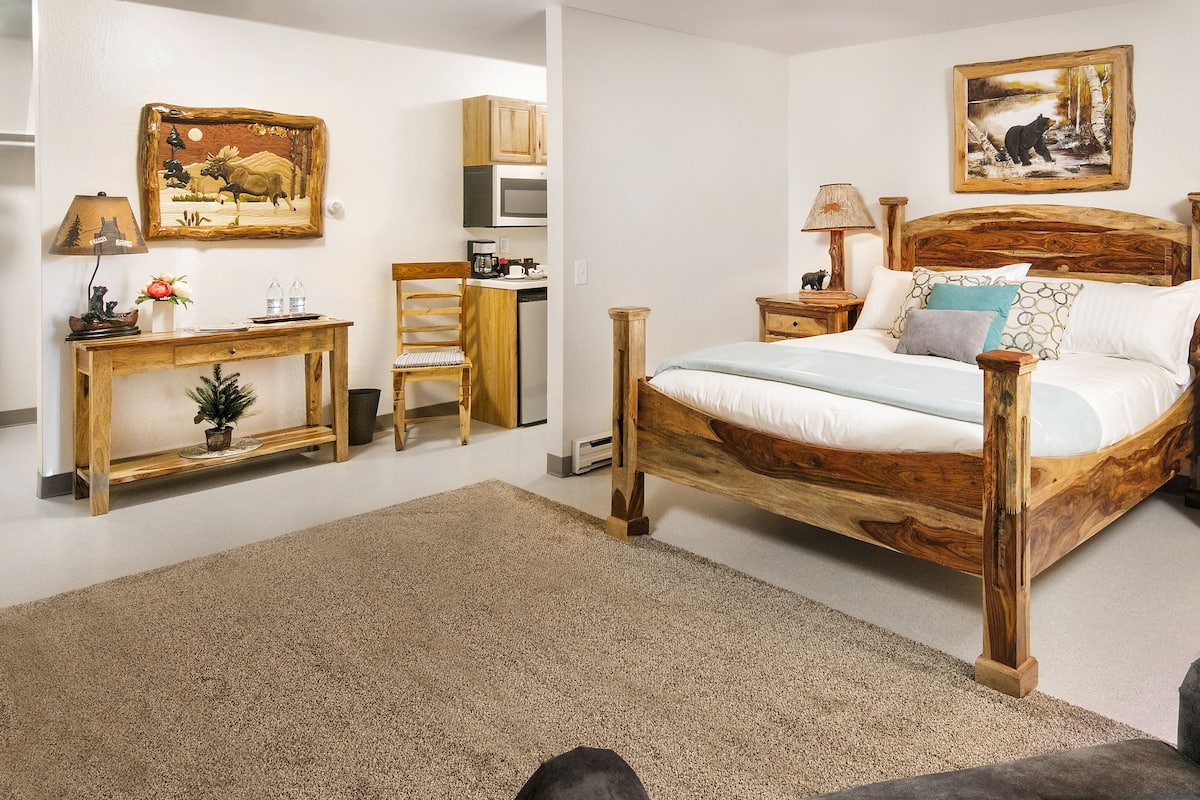 A bedroom with a wooden bed, bedside tables, a desk, and a chair. There are two paintings on the walls.