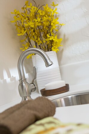 A bathroom sink with a modern faucet, a vase with yellow flowers, and a brown soap dish.