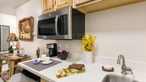 A modern kitchen with wooden cabinets, a stainless steel microwave, a sink, and a vase with yellow flowers. - Mat-Su Resort (Wasilla)