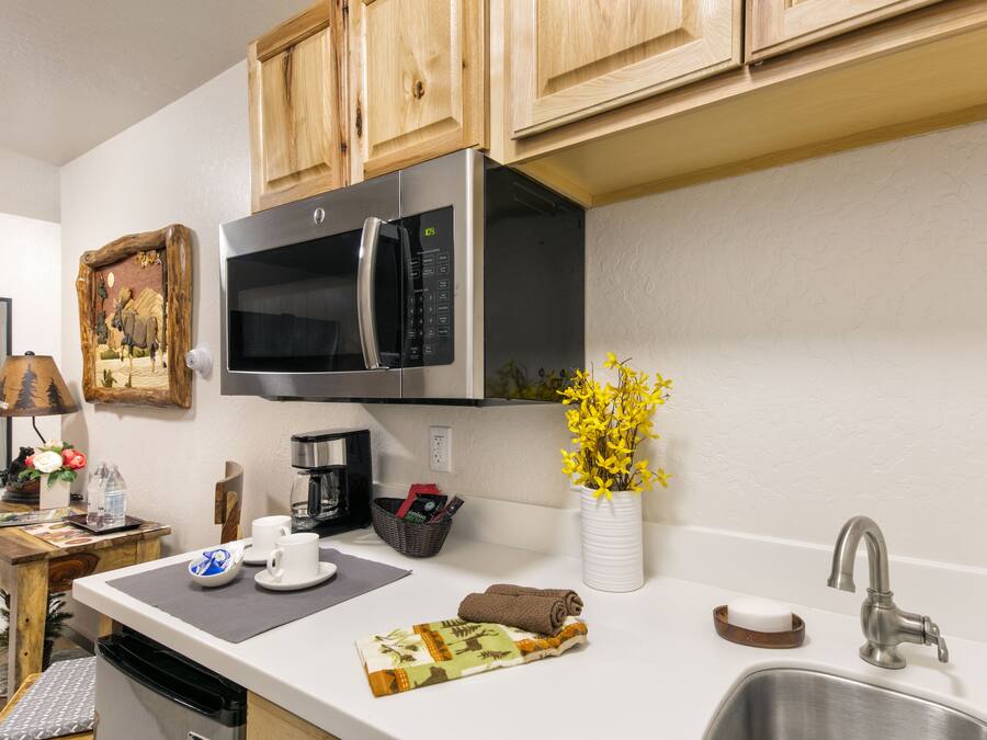 A modern kitchen with wooden cabinets, a stainless steel microwave, a sink, and a vase with yellow flowers.