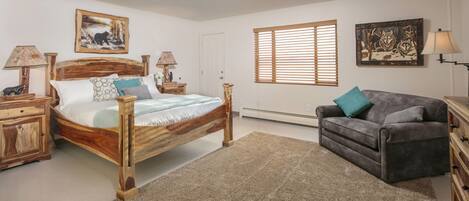 A bedroom with a wooden bed, two nightstands, a gray sofa, and a window with blinds.
