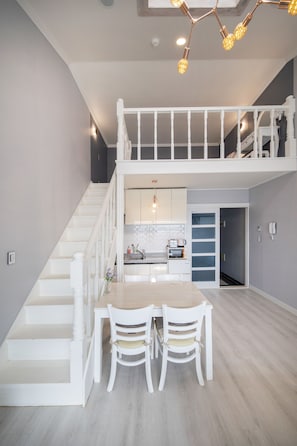 Amplia sala de estar con una escalera que conduce a un segundo piso, una mesa de comedor con sillas y una cocina equipada con electrodomésticos modernos.