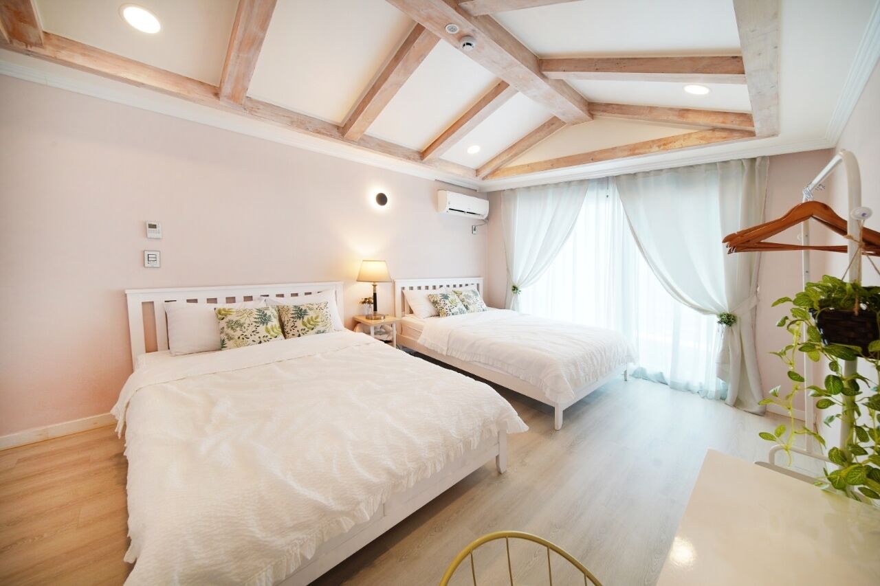 Une chambre avec deux lits, des poutres en bois au plafond, une table de chevet avec une lampe et une plante suspendue.