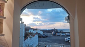 Vista a través de un arco de entrada a un estacionamiento con coches, un pabellón y una puesta de sol sobre el mar.