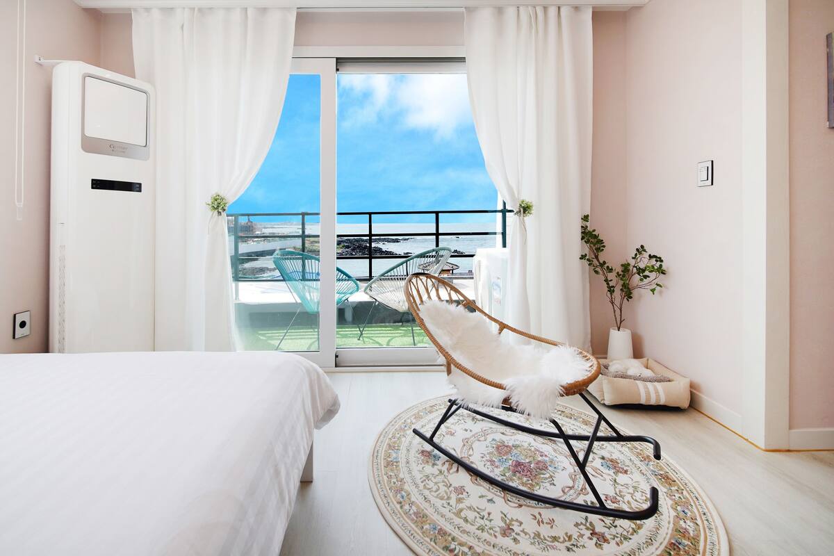 A hotel room with a bed, a rocking chair, a small table, and a view of the sea through a balcony.