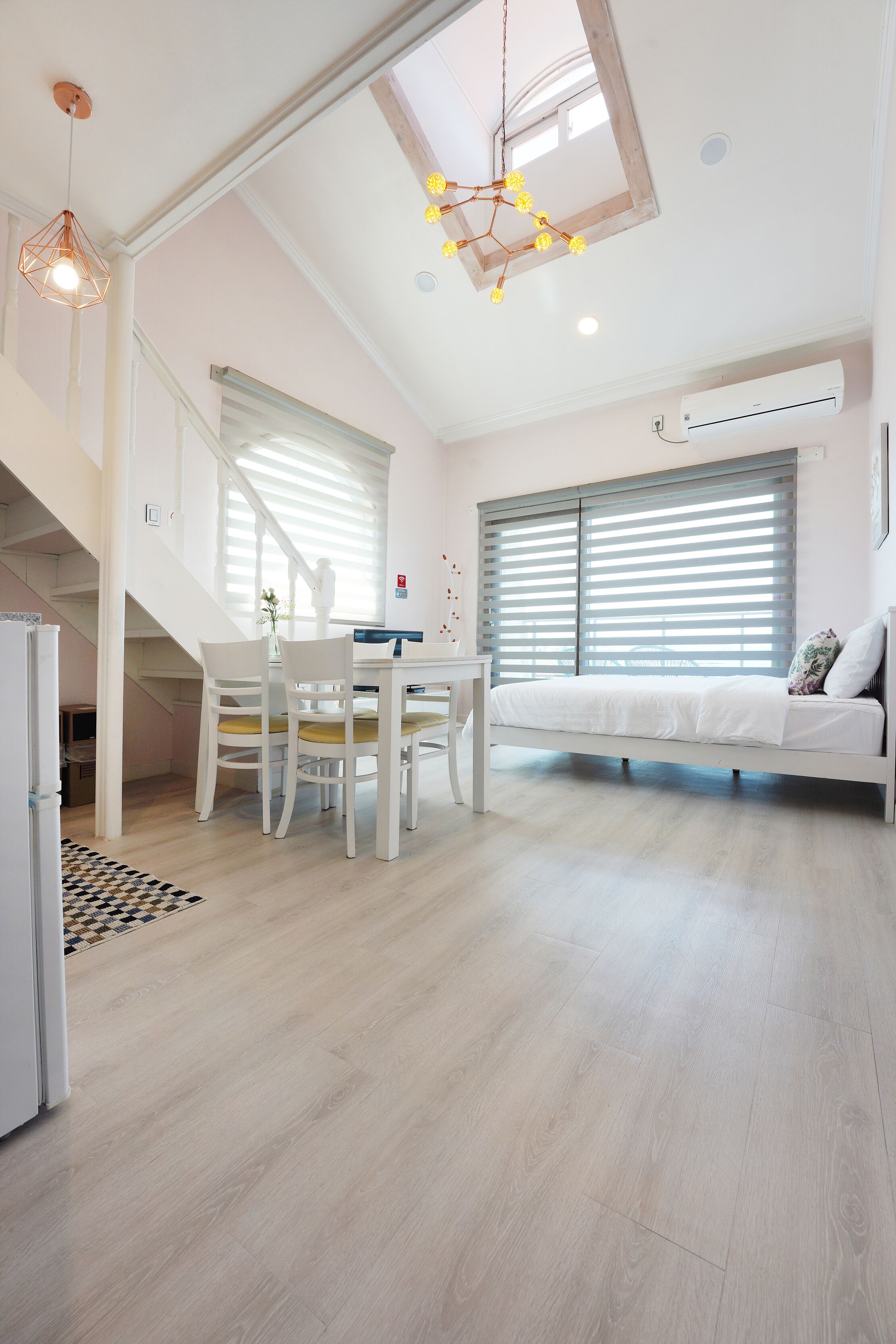 A spacious room with a bed, a dining table with chairs, a staircase, and a ceiling light fixture.