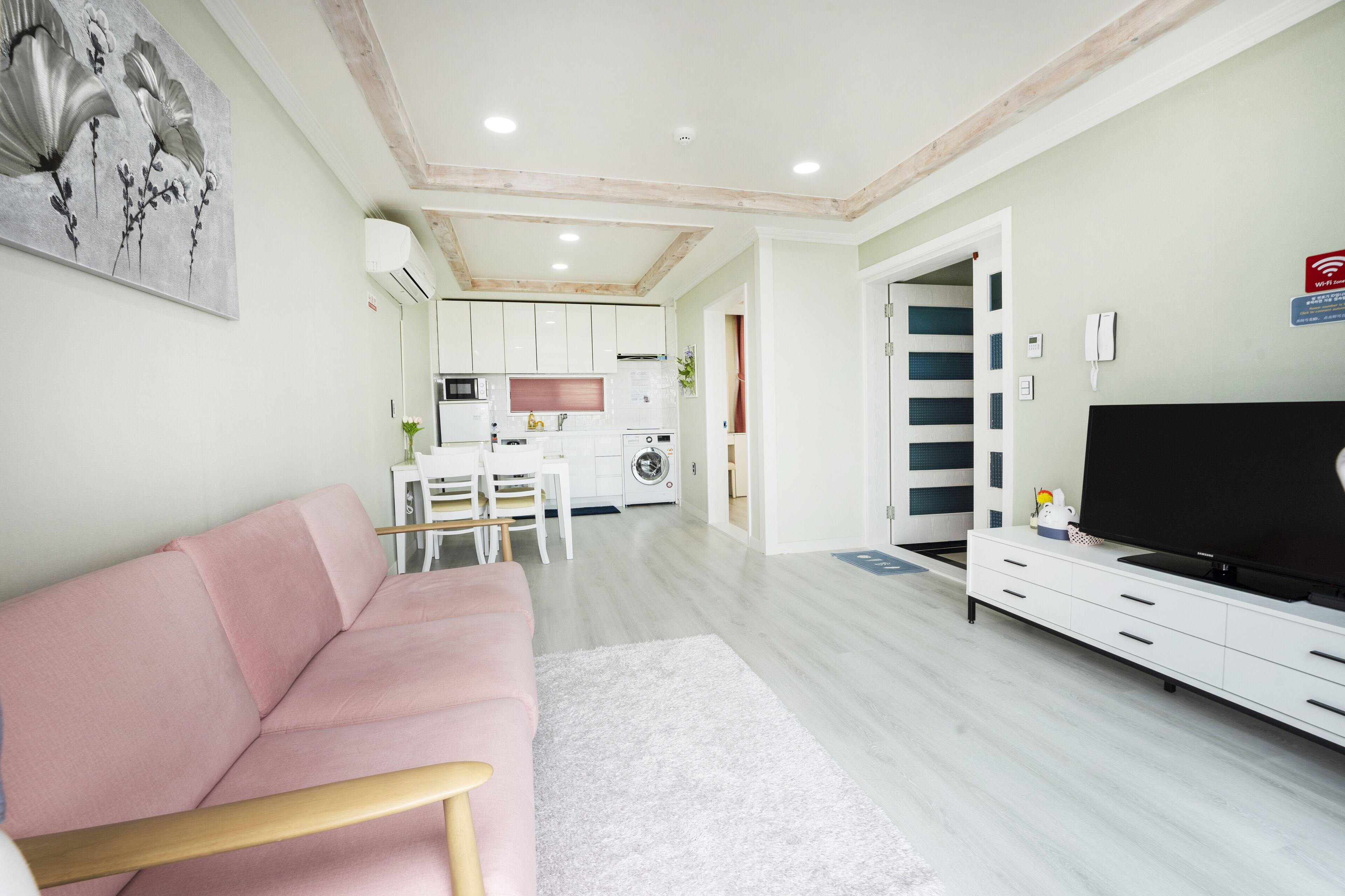 A modern living room with a pink sofa, a flat-screen TV, and a dining area with a white table and chairs.