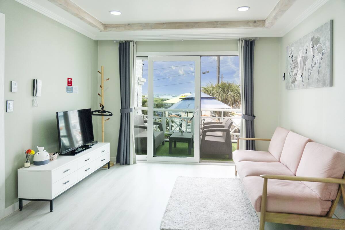 A modern living room with a flat-screen TV, a white sofa, and a sliding glass door leading to an outdoor patio.