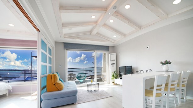 Una sala de estar moderna con un sofá, un comedor con sillas, un televisor y vista al mar.