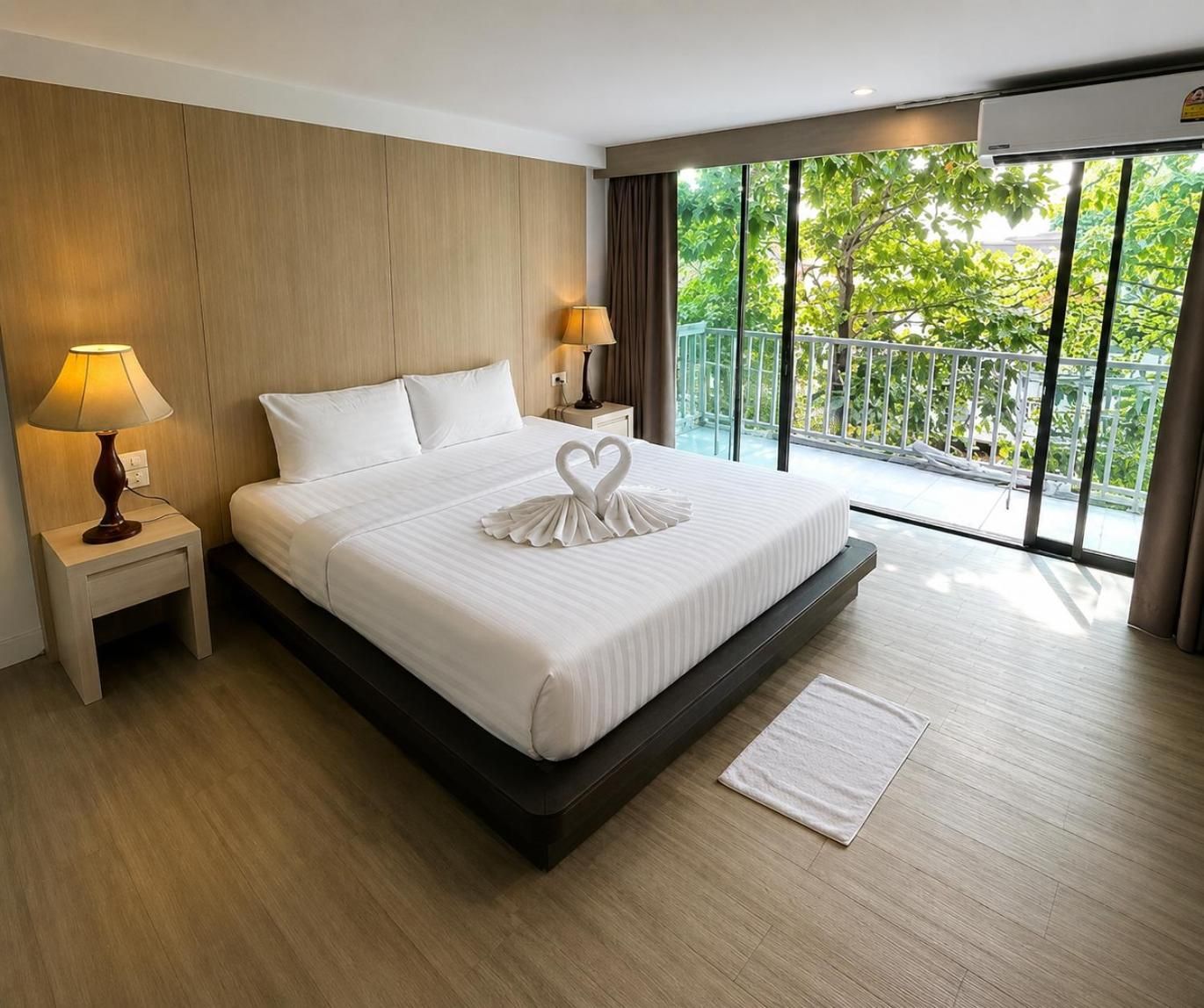 A hotel room with a large bed, two bedside lamps, a view of greenery through the window, and a balcony.