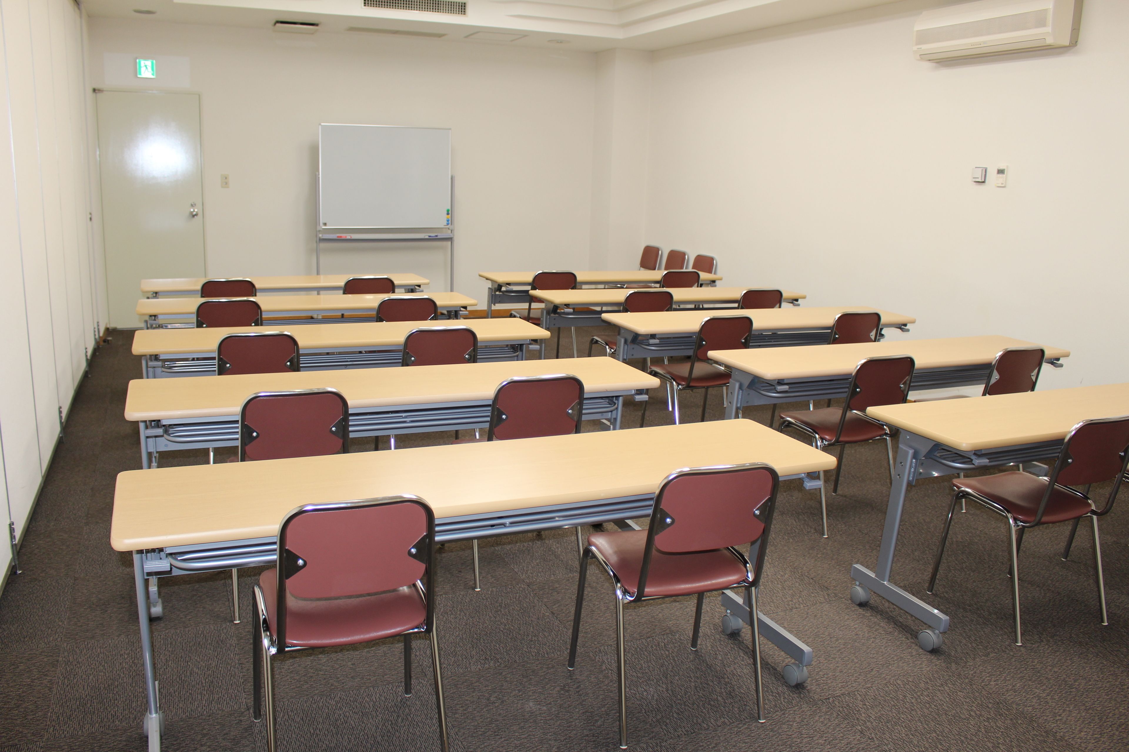 A classroom with rows of desks and chairs, a whiteboard, and an exit door.