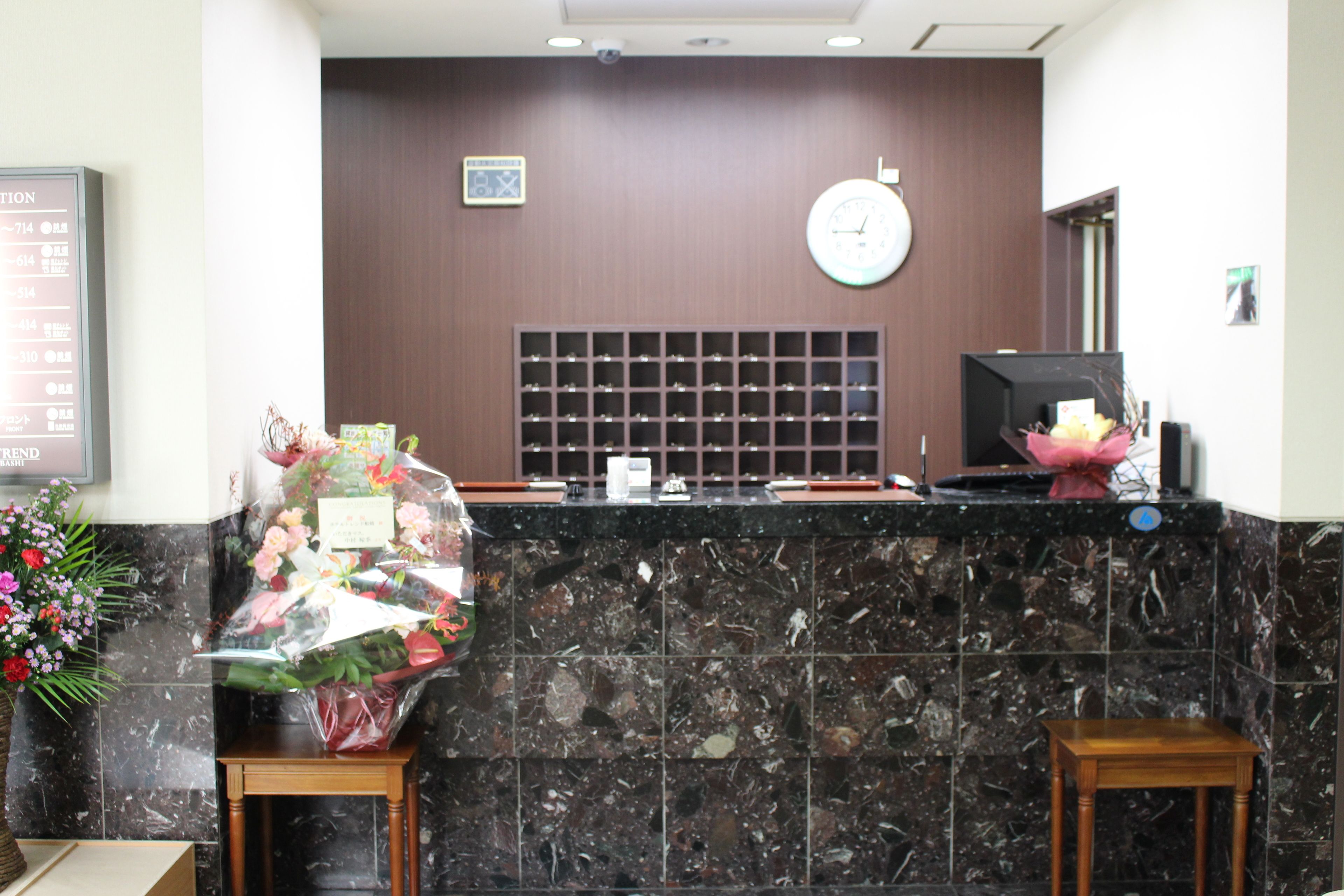 A hotel reception area with a marble counter, a clock, a bulletin board, and a floral arrangement.