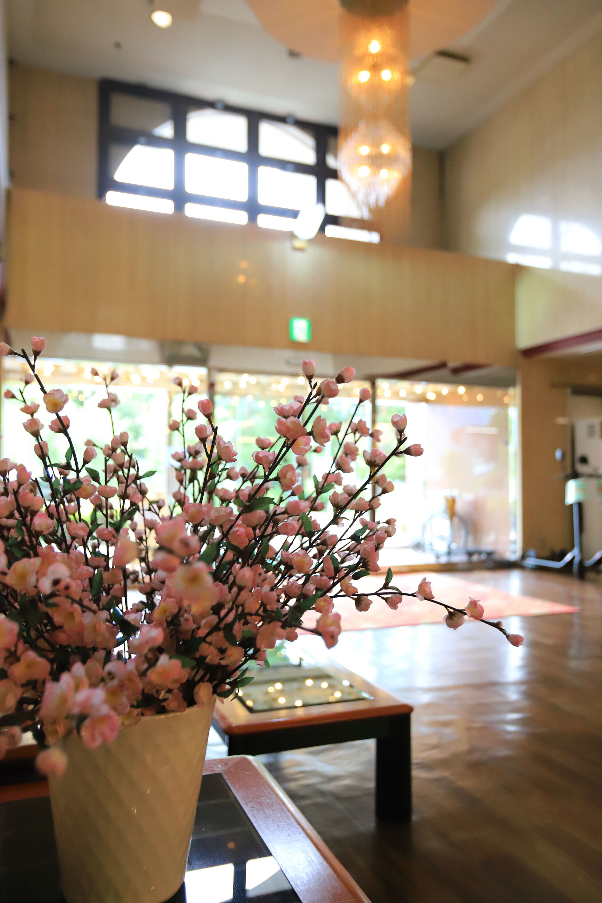 A lobby area with a reception desk, a vase with pink flowers, and a chandelier.