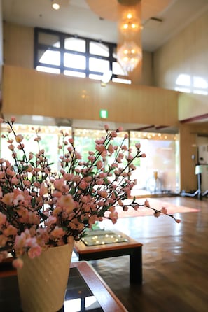 Un espace d’accueil avec un comptoir de réception, un vase rempli de fleurs roses et un lustre.