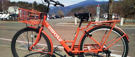 Una bicicletta rossa con cestino e sellino, parcheggiata su una strada con montagne sullo sfondo.
