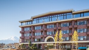 Un hotel de varios pisos con una entrada arqueada destacada, ventanas amplias y una montaña al fondo.