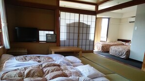 Une pièce de style japonais traditionnel, avec un sol recouvert de tatamis, un futon servant de lit, une télévision et des portes coulissantes en papier de riz (shoji).