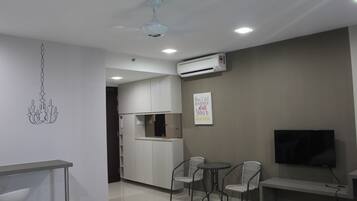 A modern living room with a dining area, a TV mounted on the wall, and an air conditioning unit.