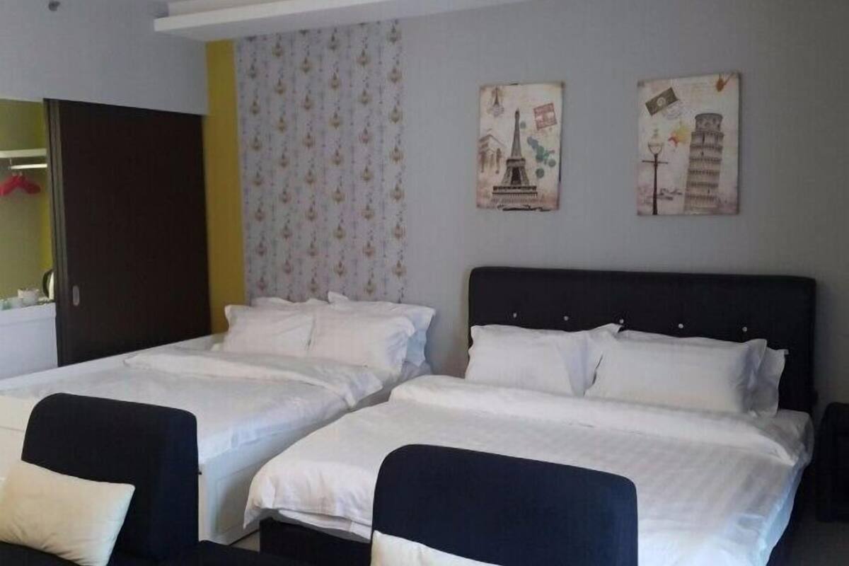 Une chambre d’hôtel avec deux lits, une tête de lit sombre et un rideau orné d’un motif floral.
