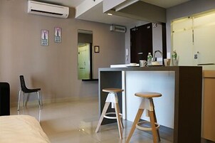 A modern hotel room with a bed, a desk, two stools, an air conditioning unit, and a door leading to another room.