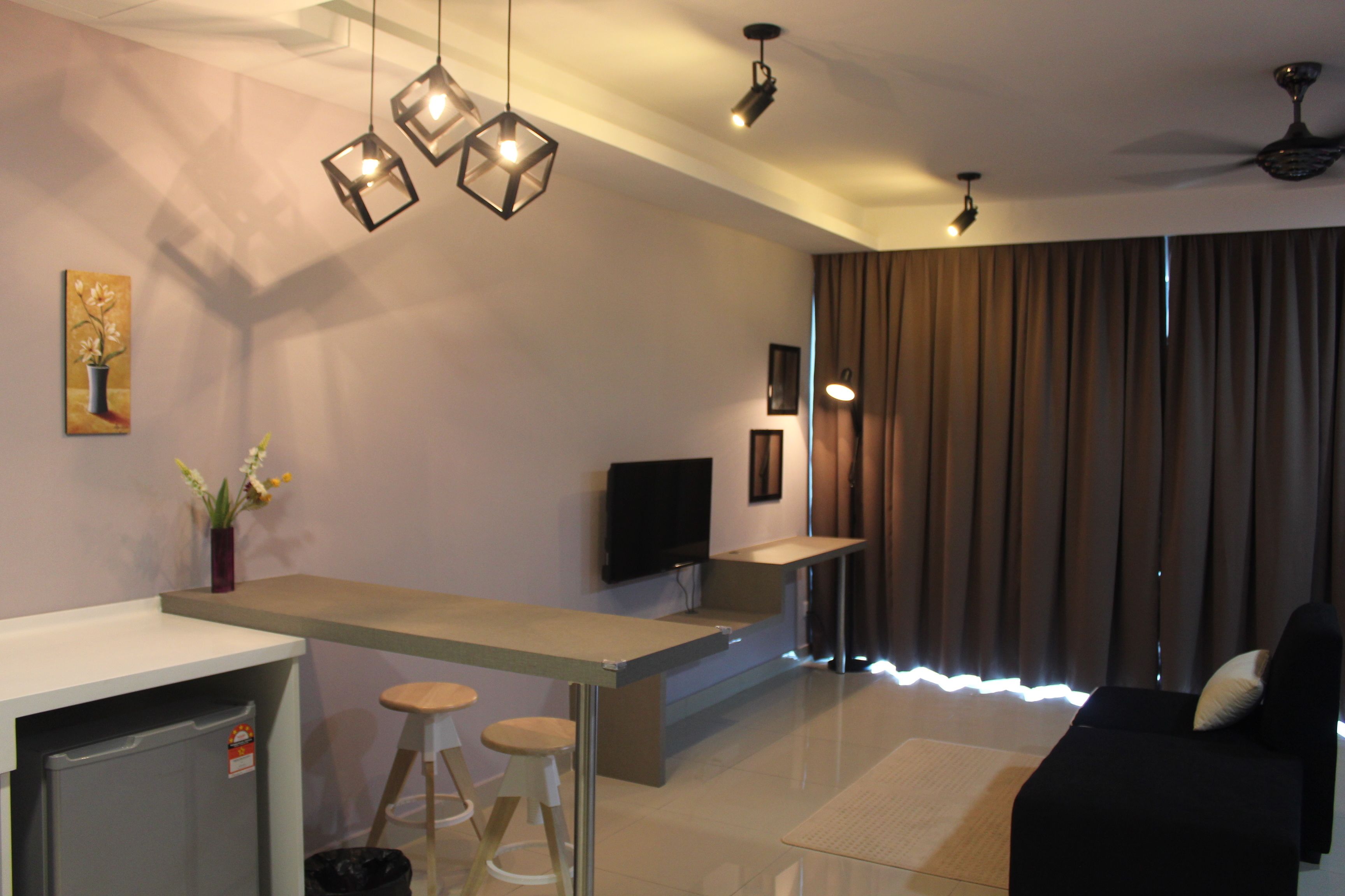 A modern living room with a flat-screen TV, a sofa, a coffee table, and a kitchen area with stools.